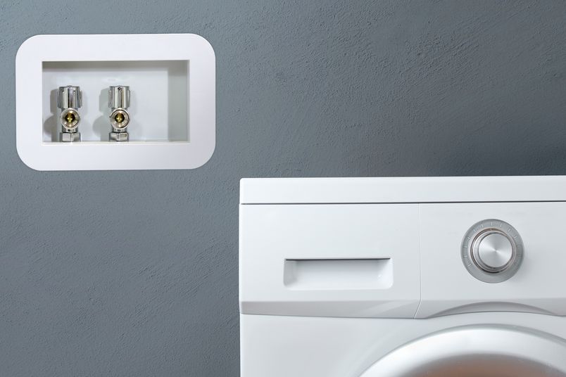 A laundry outlet box by Allproof Industries, installed next to a washing machine.